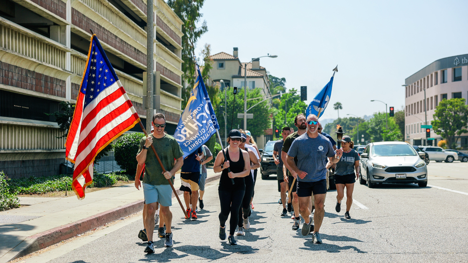 A group of participants run in formation carrying the torch and flags during an event for the Special Olympics