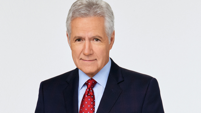 A photo of Alex Trebek wearing a dark jacket and red tie