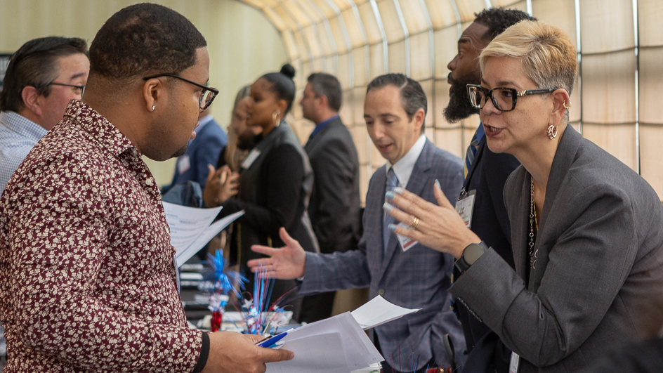 Career conference attendees speak to each other across tables.