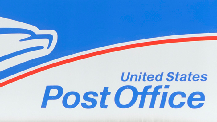 A United States Post Office sign hangs on a red brick wall
