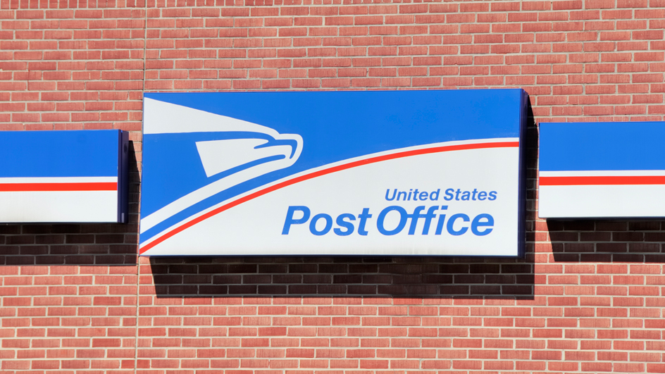 A United States Post Office sign hangs on a red brick wall