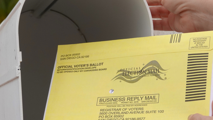 An official ballot being placed into a mailbox.