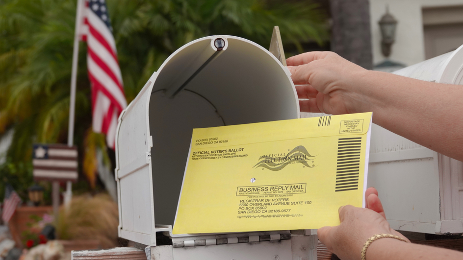 An official ballot being placed into a mailbox.