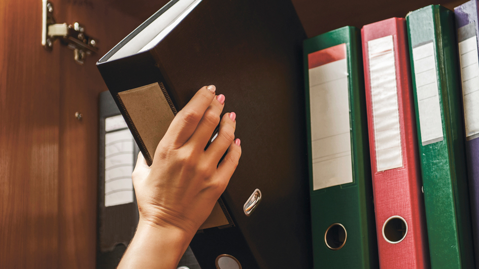 A hand lifts one binder from a colorful set containing records