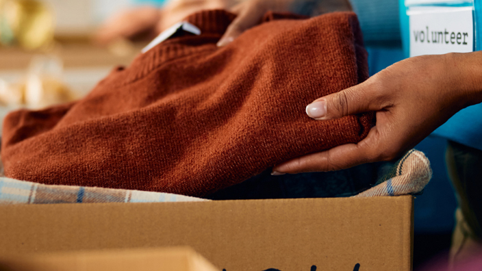 A volunteer places a reddish-orange sweater into a box