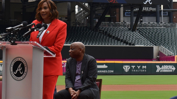 People in business wear sit on baseball diamond during ceremony