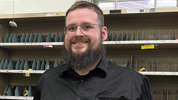 Smiling man stands in postal workroom