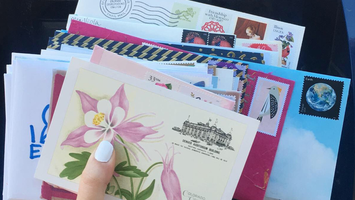 A woman's hand holds a bundled of stamped envelopes containing hand-written letters