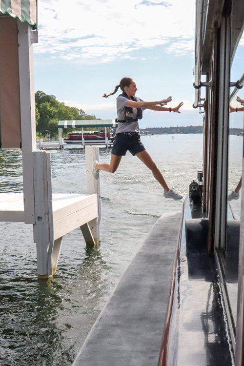 A woman jumps from a dock onto a boat.