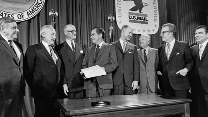 Six former postmasters general and incumbent Postmaster General Winton M. Blount were present when President Richard M. Nixon signed the Postal Reorganization Act on Aug. 12, 1970. From left are John A. Gronouski, J. Edward Day, James A. Farley, Nixon, Blount, Arthur E. Summerfield, Lawrence F. O’Brien and W. Marvin Watson.