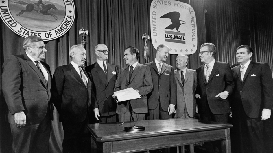 Six former postmasters general and incumbent Postmaster General Winton M. Blount were present when President Richard M. Nixon signed the Postal Reorganization Act on Aug. 12, 1970. From left are John A. Gronouski, J. Edward Day, James A. Farley, Nixon, Blount, Arthur E. Summerfield, Lawrence F. O’Brien and W. Marvin Watson.