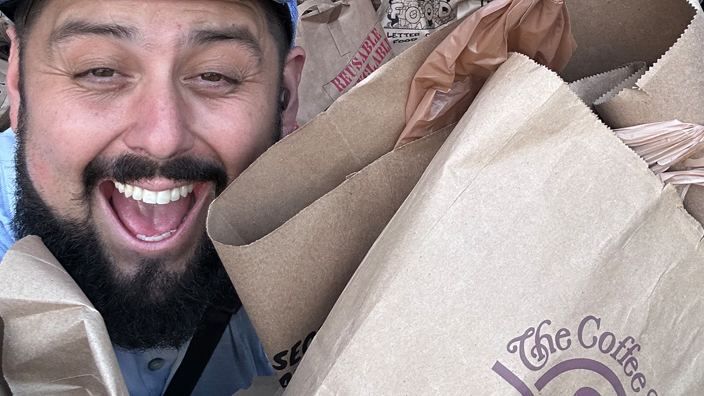 A smiling man carries several brown paper bags filled with donated food.