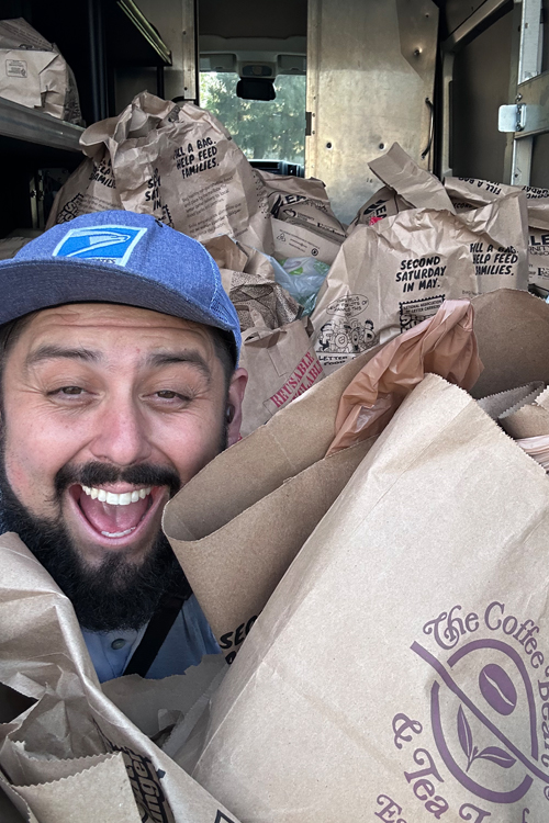 A smiling man carries several brown paper bags filled with donated food.