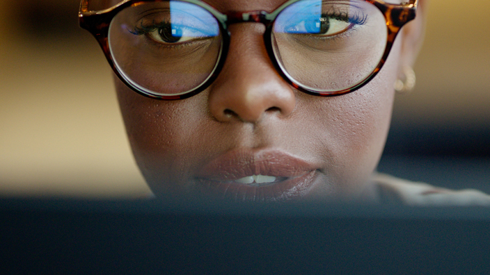 A woman wearing glasses looks down at a laptop computer screen.