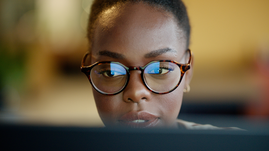 A woman wearing glasses looks down at a laptop computer screen.