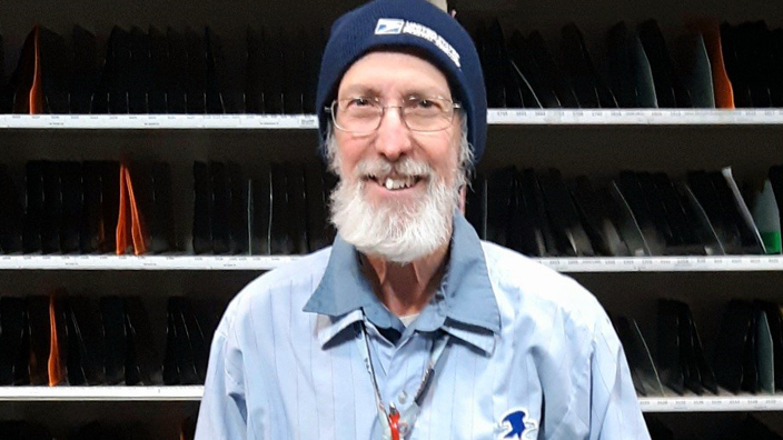 USPS Letter Carrier Gerald Loney stands in front of a sorting rack