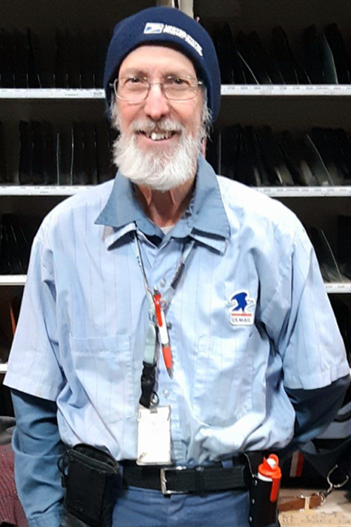 USPS Letter Carrier Gerald Loney stands in front of a sorting rack