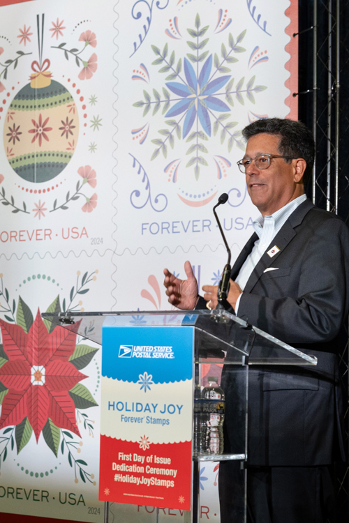 USPS art director Antonio Alcala stands at a lectern with the large-size image of the USPS Holiday Joy stamps behind him.