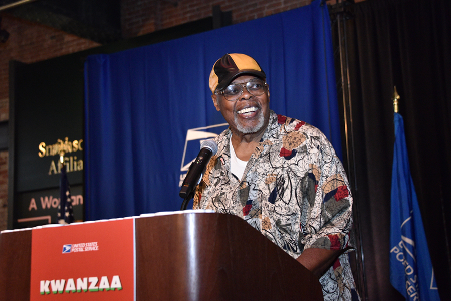 Sala Udin, wearing a cap, speaks from behind a lectern.