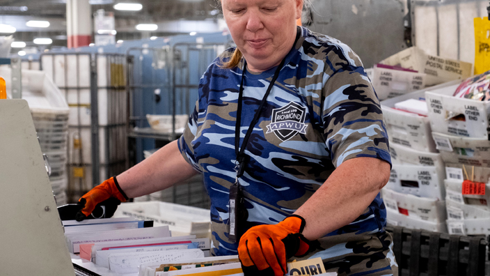 A USPS employee handles mail in a sorting and distribution facility.