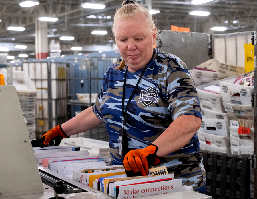 A USPS employee handles mail in a sorting and distribution facility.