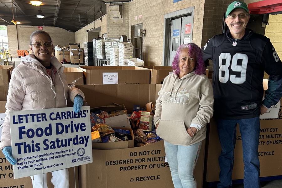 Three women stand in front of boxes of donated food items.