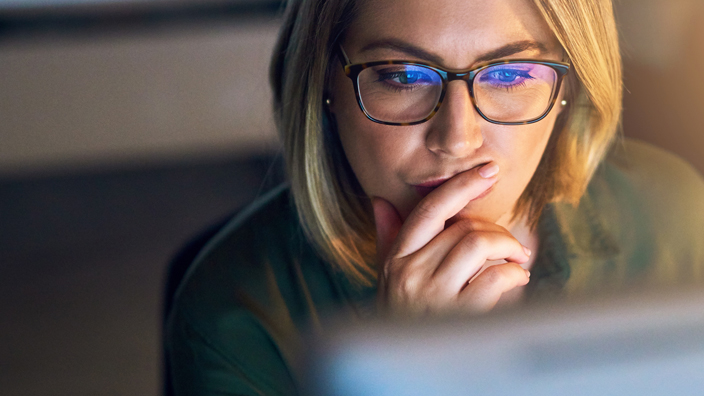 A woman ponders as she peers at a computer screen