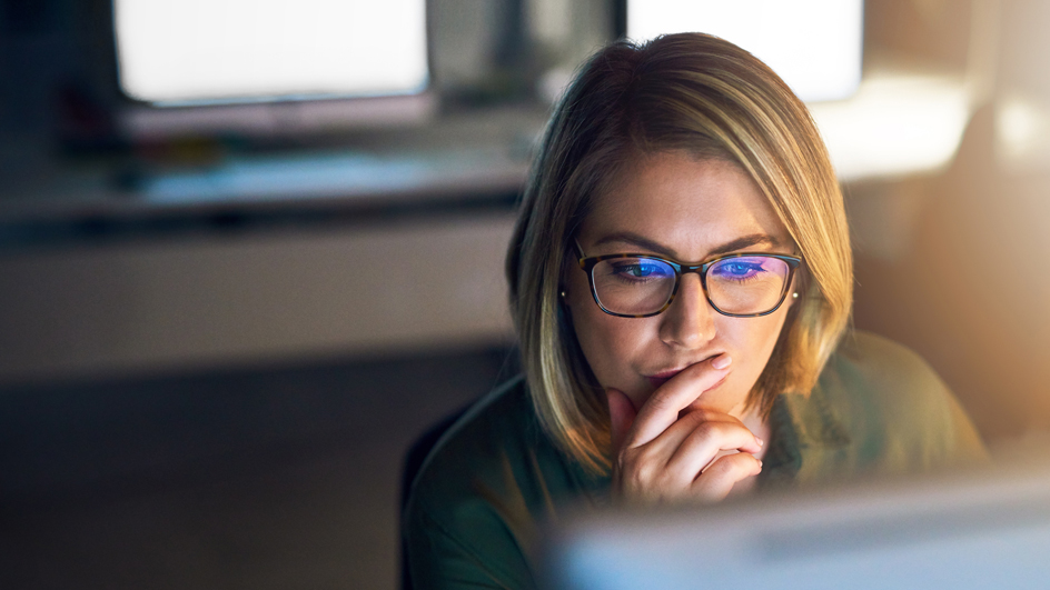 A woman ponders as she peers at a computer screen