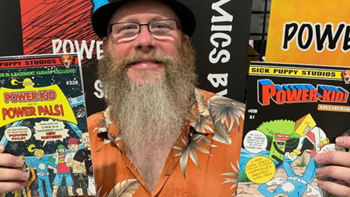 A man with a beard and eyeglasses holds a comic book.