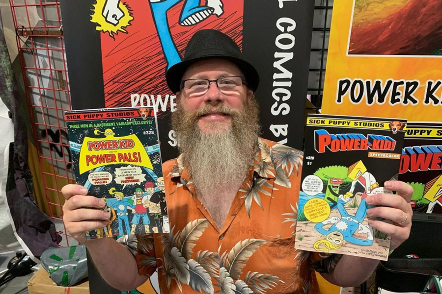 A man with a beard and eyeglasses holds a comic book.