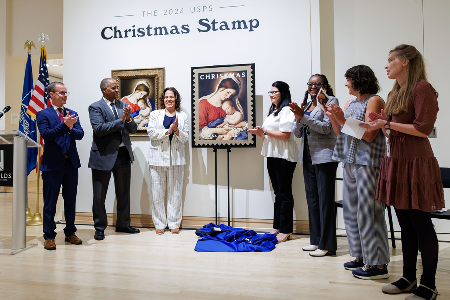 A group of people stand on either side of an enlarged image of the USPS Christmas Madonna and Child stamp