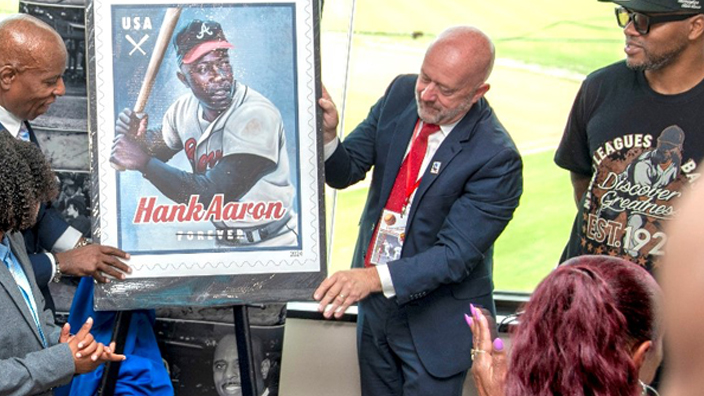 Dwayne Renal Sims, founder of a nonprofit group that promotes the history of baseball’s Negro League, left, and Mark Wahl, a USPS strategic communications specialist, unveil the Hank Aaron stamp image at a recent ceremony in Bowie, MD.