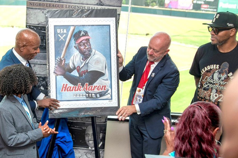 Dwayne Renal Sims, founder of a nonprofit group that promotes the history of baseball’s Negro League, left, and Mark Wahl, a USPS strategic communications specialist, unveil the Hank Aaron stamp image at a recent ceremony in Bowie, MD.