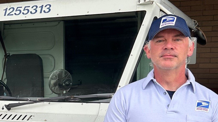 Smiling man in postal uniform stands near delivery vehicle