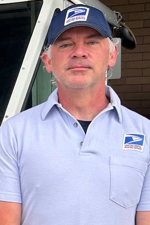 Smiling man in postal uniform stands near delivery vehicle