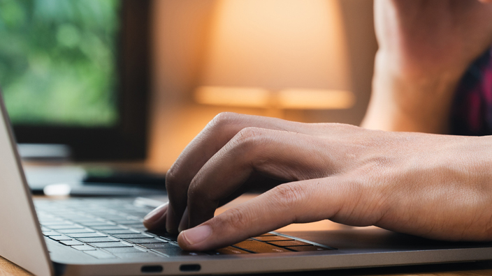 A man types on the keyboard of a laptop computer.