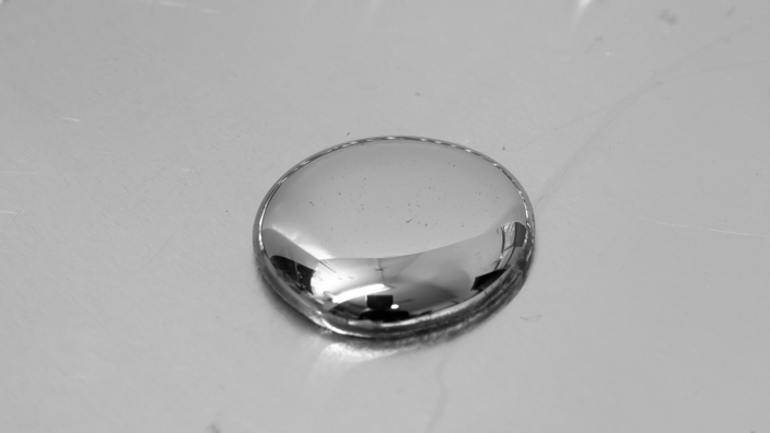 A large drop of mercury with smaller droplets of the liquid metal above it.