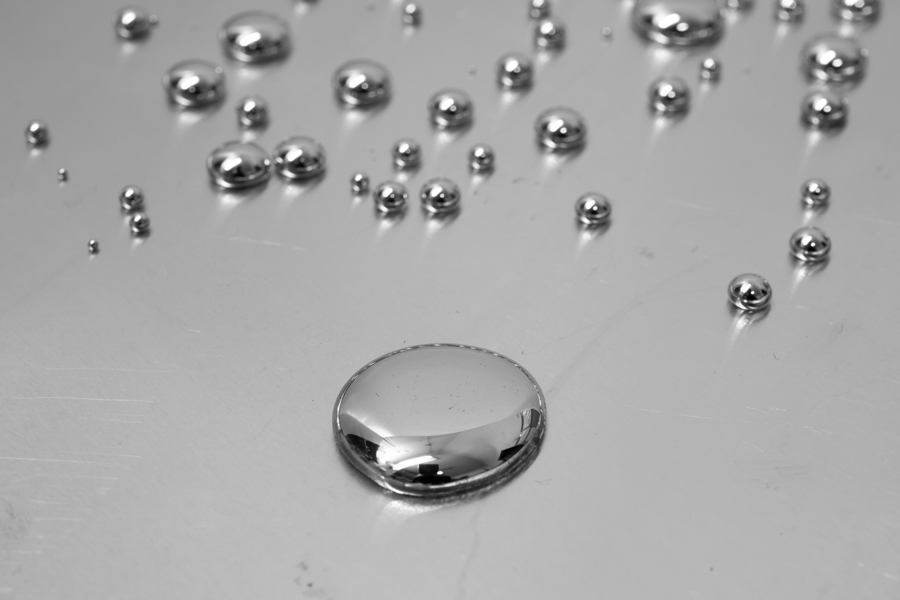 A large drop of mercury with smaller droplets of the liquid metal above it.