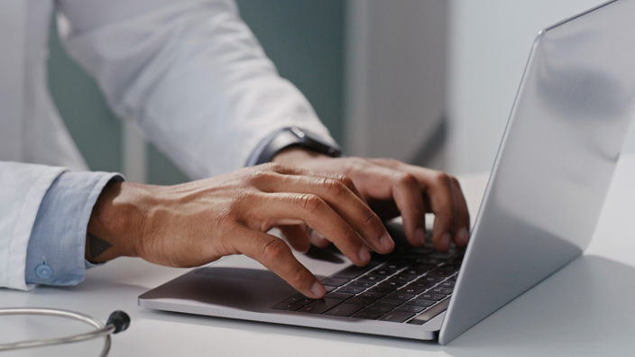 A medical professional typing on a laptop computer