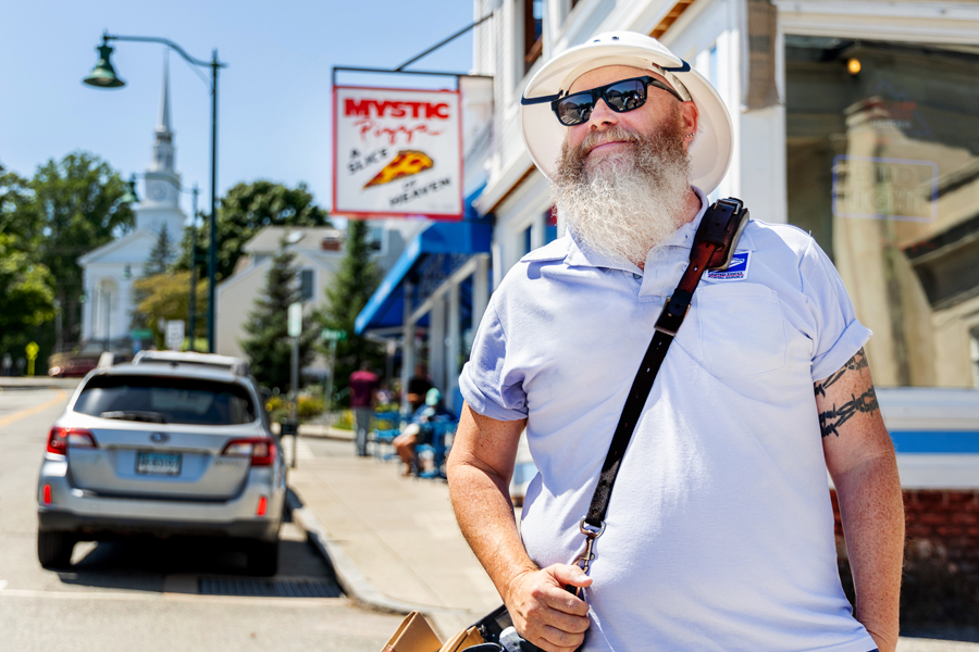 Letter Carrier Brett Swanson stands on a street in Mystic, CT.