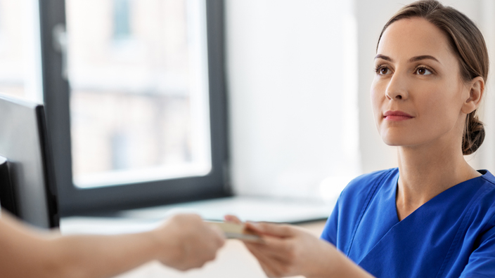 A woman wearing a blue uniform shirt at a medical office is handed a payment card.