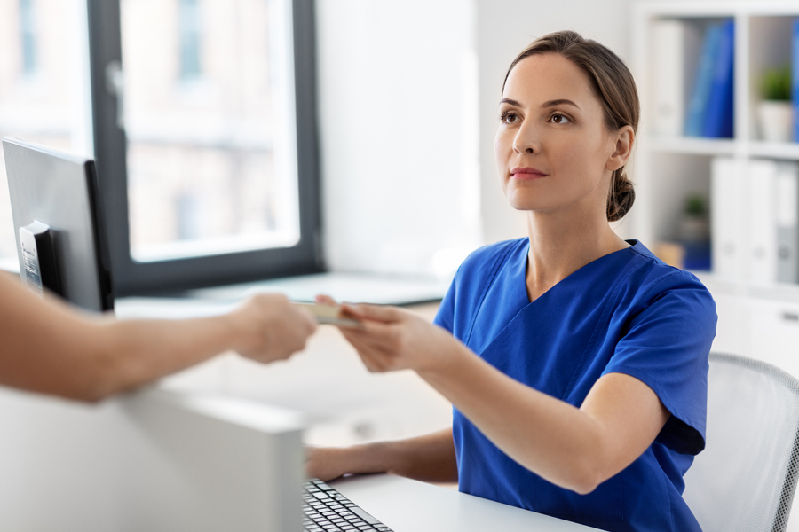 A woman wearing a blue uniform shirt at a medical office is handed a payment card.