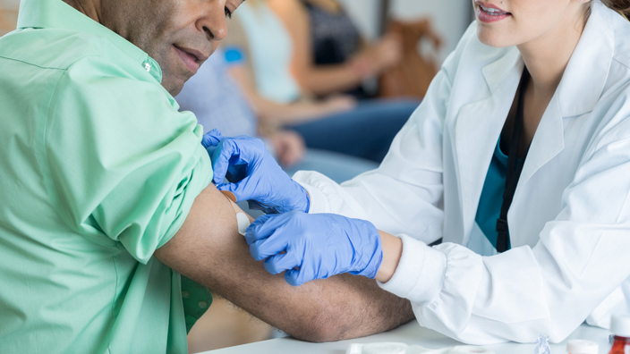 A medical professional places a bandage on the arm of a patient after receiving a flu shot