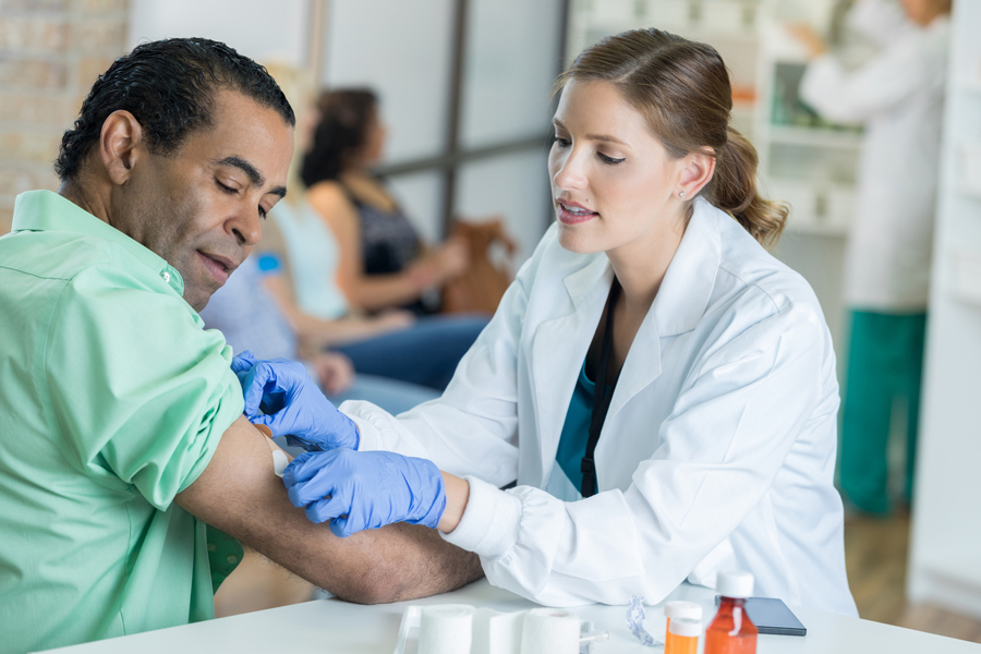 A medical professional places a bandage on the arm of a patient after receiving a flu shot