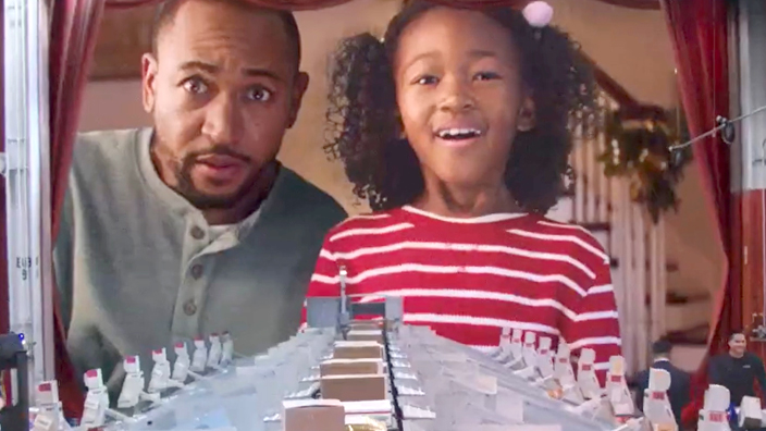 A father and daughter look down on packages moving along a conveyor belt