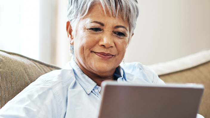 An older woman sitting on a couch looking at a tablet computer