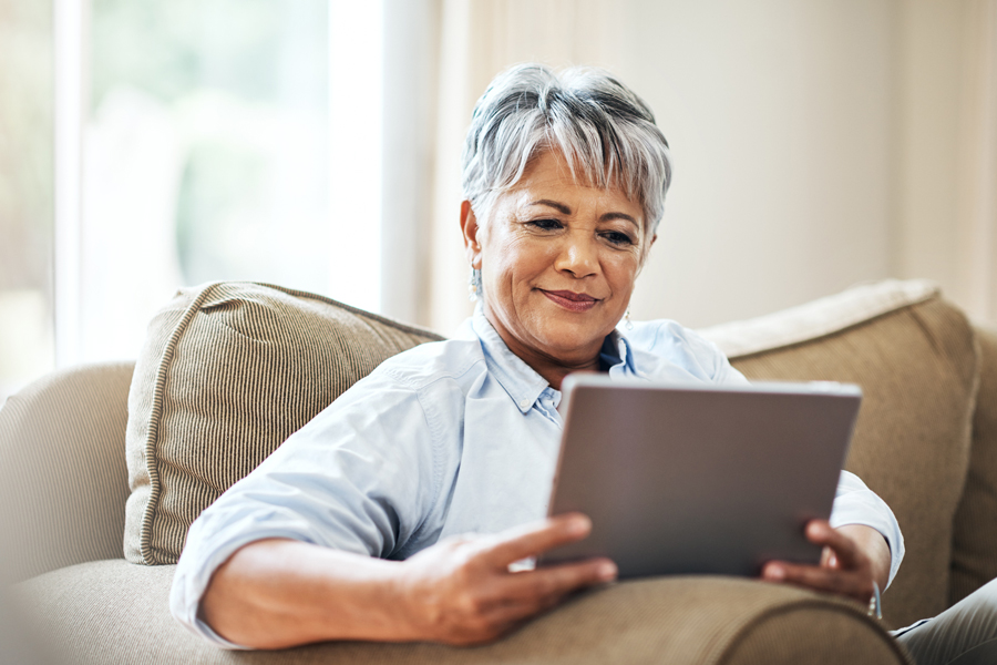 An older woman sitting on a couch looking at a tablet computer