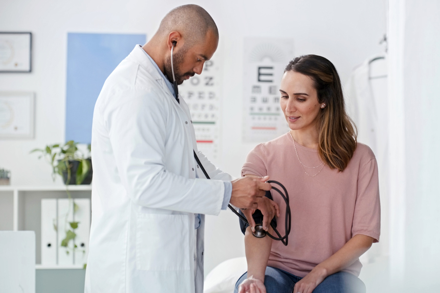 A male doctor wearing a white coat speaks with with a female patient wearing a pink shirt