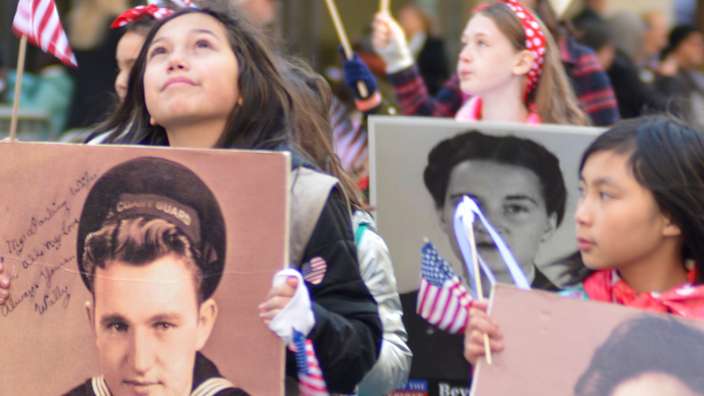 People march in a parade carrying large photos of soldiers and sailors.