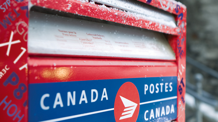 A red Canada Post mail box along a street.